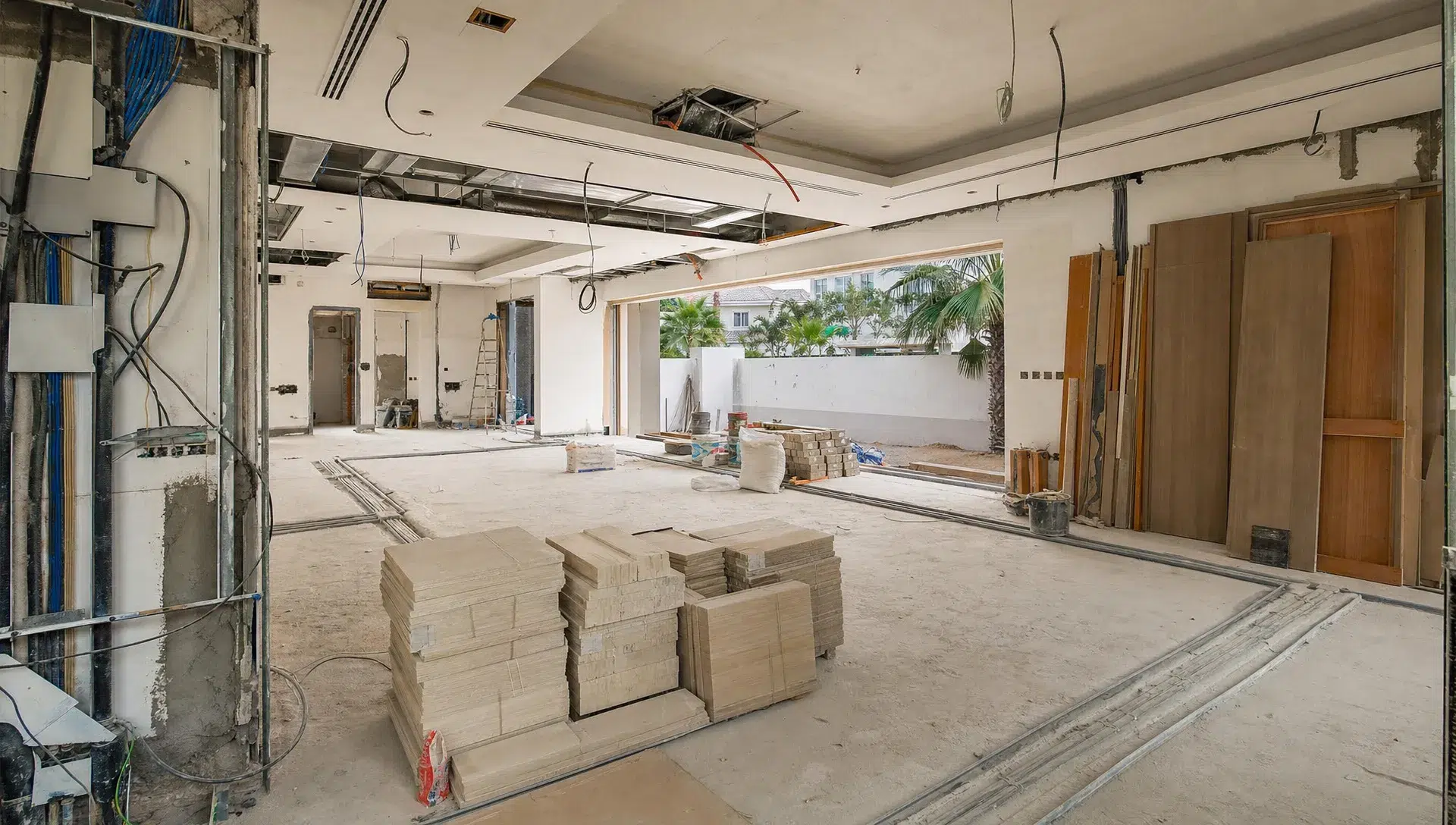 A Dubai villa interior under renovation with open walls, exposed service routes, stacked tiles, and carpentry materials organized before finishes are installed.